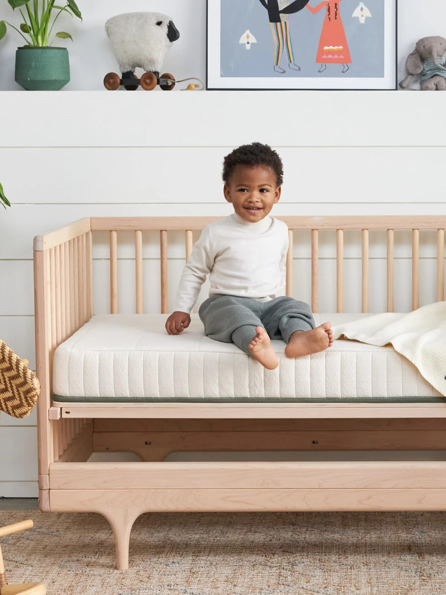 A young child sits on a Avocado crib mattress.