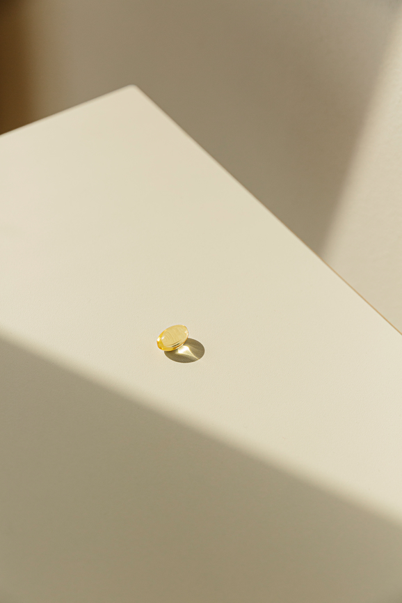 Single yellow supplement pill on white table staged in direct sunlight