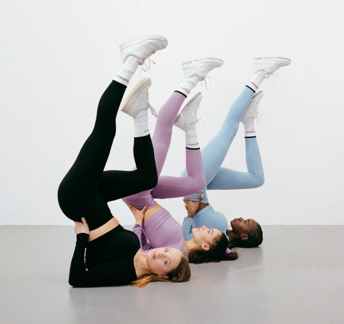 Three models laying on the floor with legs up, wearing Organic Basics cotton leggings sets.