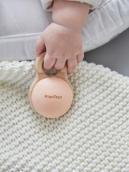 A baby holding a wooden Plantoy rattle.